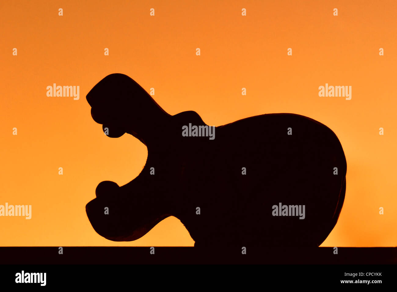 Holzskulptur des gähnenden afrikanische Flusspferd mit offenem Mund Silhouette gegen orangefarbenen Himmel bei Sonnenuntergang Stockfoto