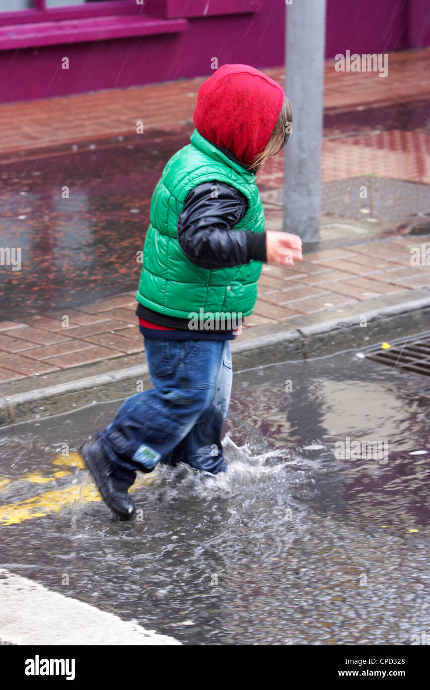 kleiner Junge Spritzer durch Pfützen in einem Regenschauer im Vereinigten Königreich Stockfoto
