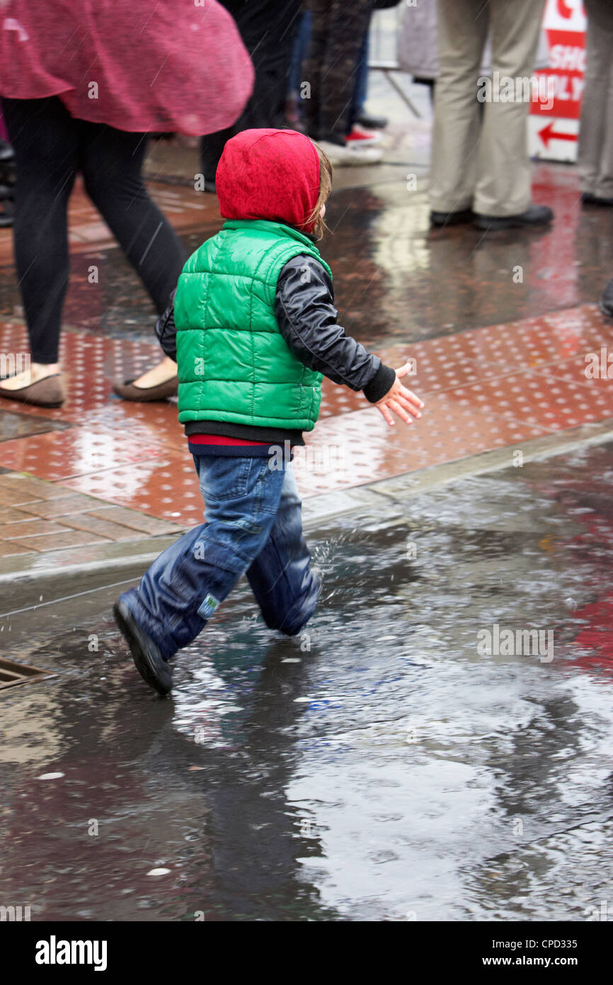 kleiner Junge Spritzer durch Pfützen in einem Regenschauer im Vereinigten Königreich Stockfoto