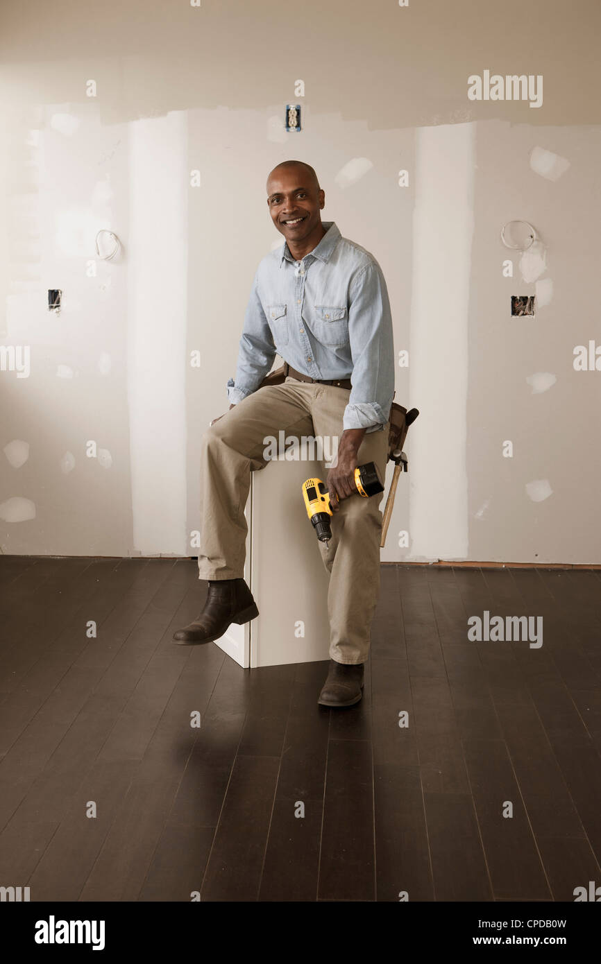 Afrikanische amerikanischer Mann, der Akku hält Bohren in unfertigen Zimmer Stockfoto