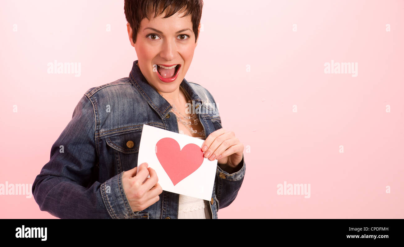 Eine hübsche Frau gegen rosa halten sie ihren Valentinstag Karte mit Herz Stockfoto