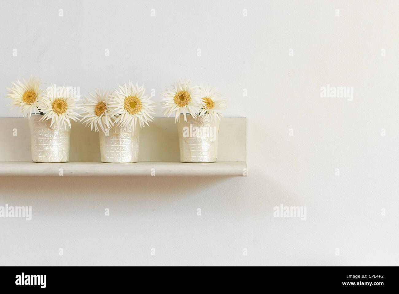 Künstliche Blumen In einer Reihe gegen weiße Wand Stockfoto