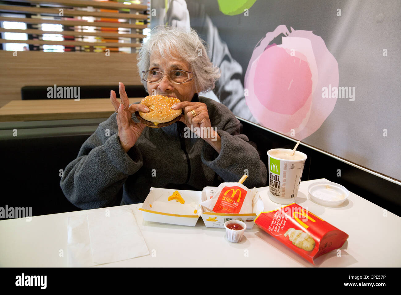 Eine ältere weiße behaarte Dame genießen Essen einen McDonalds Burger, UK Stockfoto