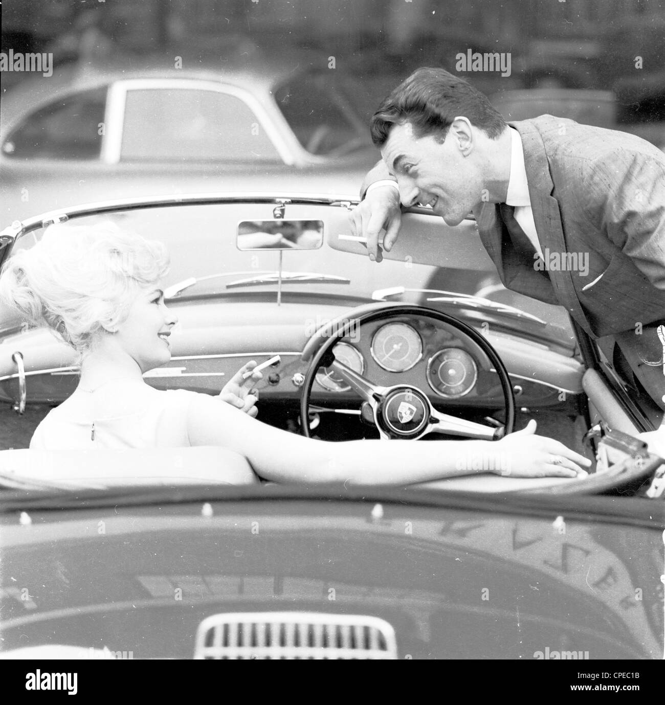1960er Jahre Foto eines jungen Paares bei offenem Verdeck Sportwagen mit der jungen Dame auf Beifahrersitz. Das Paar sind beide Raucher Stockfoto