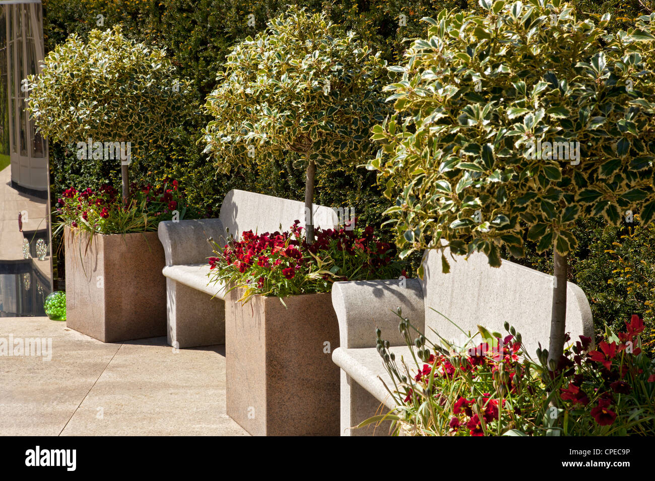 zeitgenössischen modernen Garten mit poliertem Stein Pflanzgefäße gepflanzt mit bunten Stechpalmen ein Rotes Stiefmütterchen und Steinbänken Stockfoto