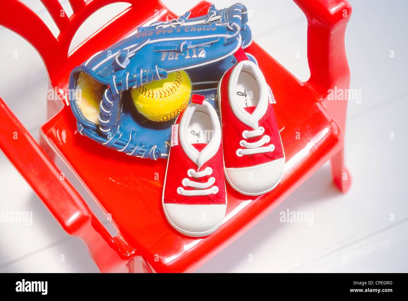Babyschuhe, Baseball und Baseballhandschuh auf roten Stuhl Stockfoto