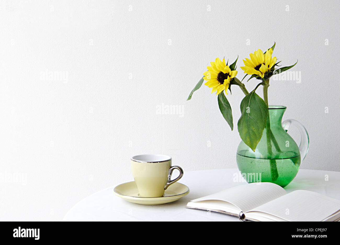 Blume im Krug, Buch- und Teetasse auf Tisch Stockfoto