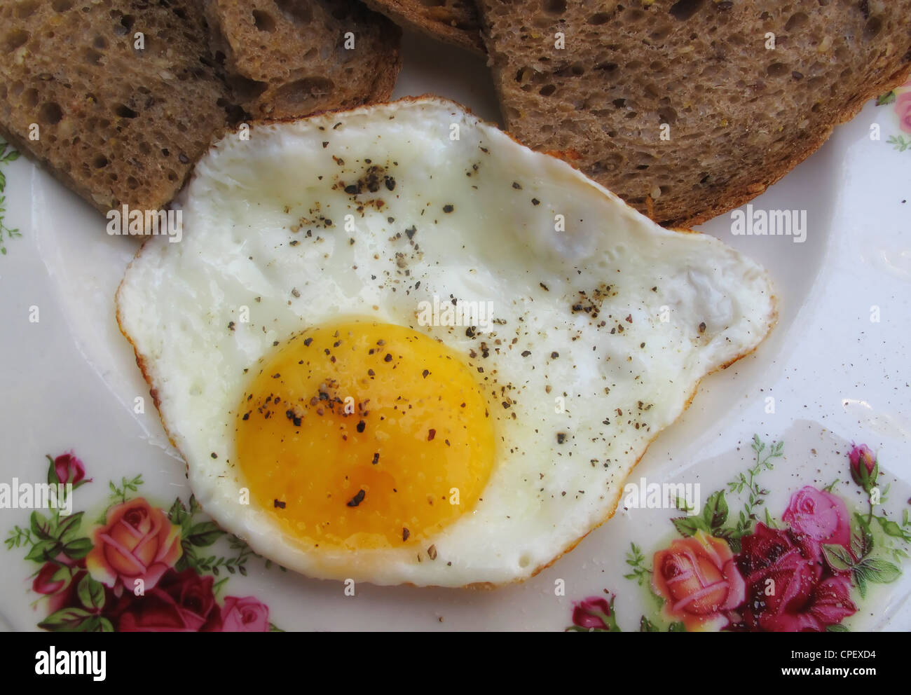 Ein Spiegelei "Sunny Side up" mit Pfeffer und Schwarzbrot auf Porzellanteller Stockfoto