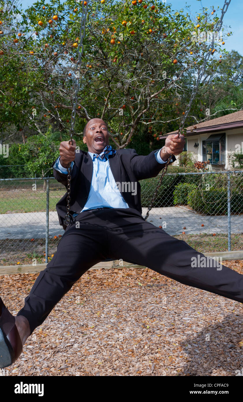 Schwarze afrikanische amerikanischer Mann in 40er Jahren gekleidet in Business-Anzug so viel Spaß auf Schaukel im Park mit keine Business-stress Stockfoto