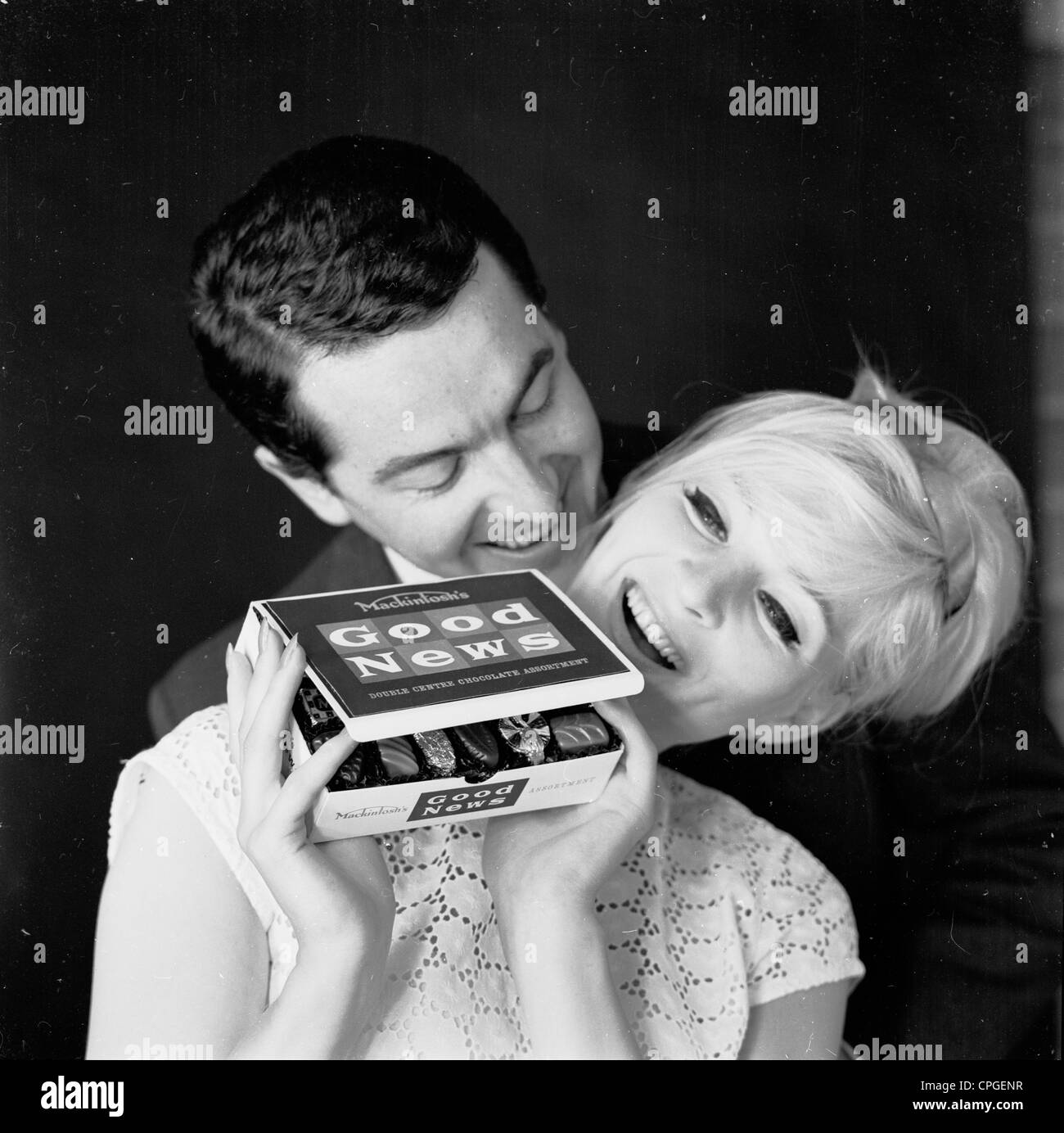 Paar nah erhalten. Frau erfreut, einen Kasten "gute Neuigkeiten" erhalten. Der 1960er Jahre. Werbung für Mackintosh's Pralinen. Stockfoto