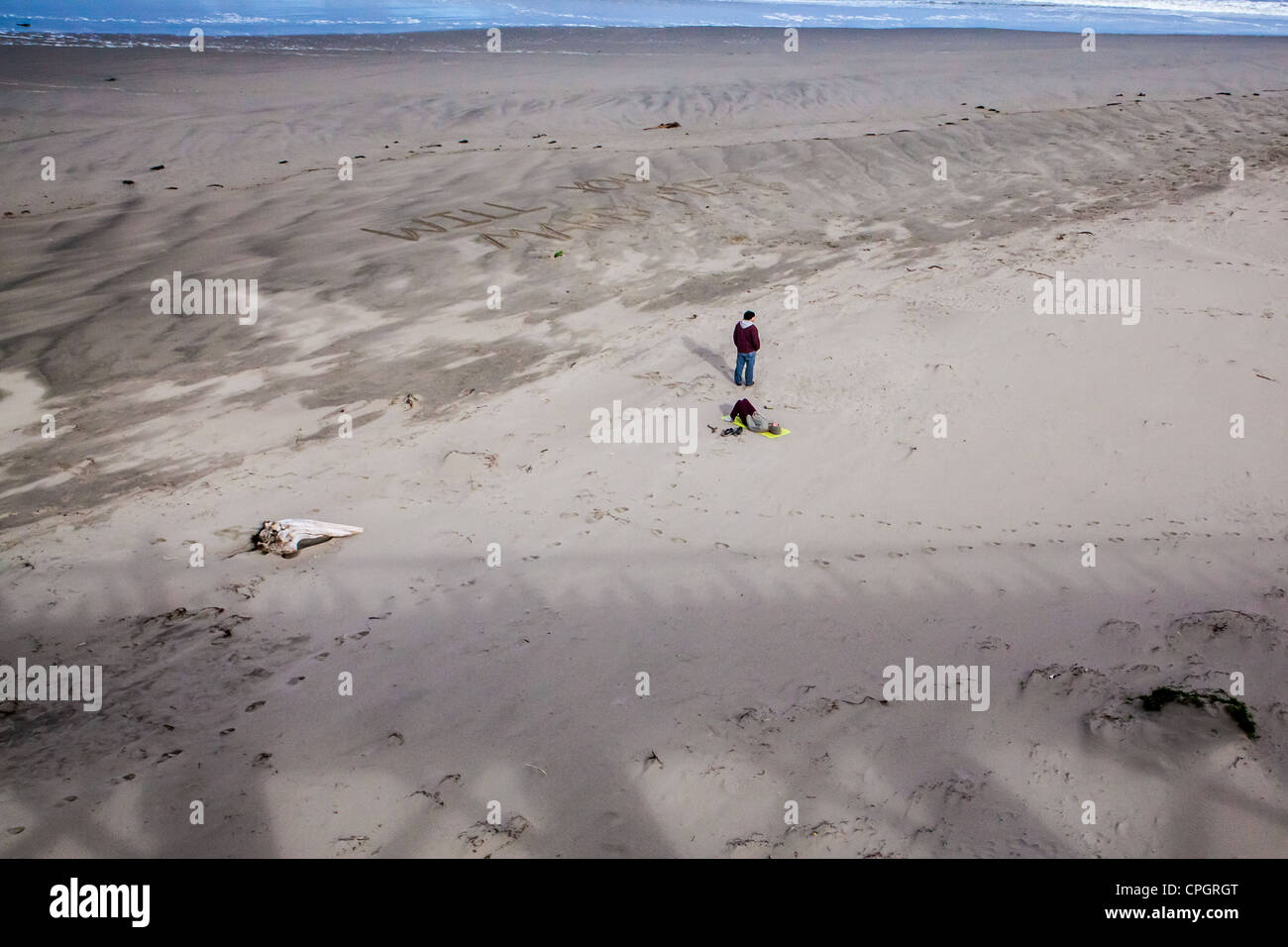 Ein junger Mann steht am Strand und betrachtet nach dem Schreiben "Sie werden mich heiraten" in den Sand in großen Lettern in Fort Bragg Ca Stockfoto