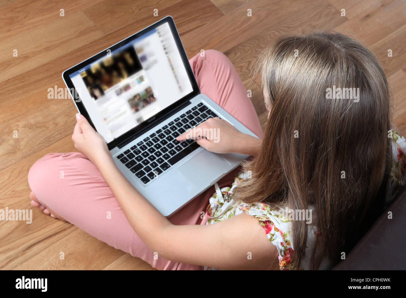 Junge Frau sitzt mit dem Rücken zur Kamera, die mit ihrem Laptop auf einer Facebook-Timeline-Seite. Stockfoto
