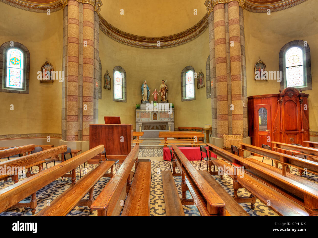 Bänke und Altar mit Skulpturen von Jesus, Maria und Joseph als Teil des Kirchenraumes in Alba, Norditalien. Stockfoto
