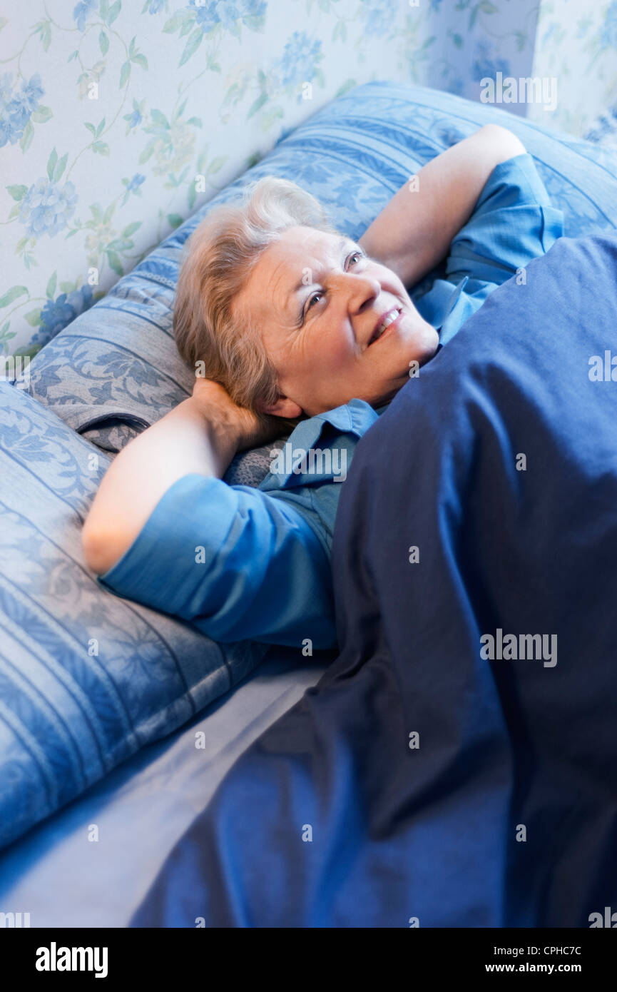 Reife Frau im Bett lag, mit ihren Händen hinter dem Kopf, breit grinsend Stockfoto