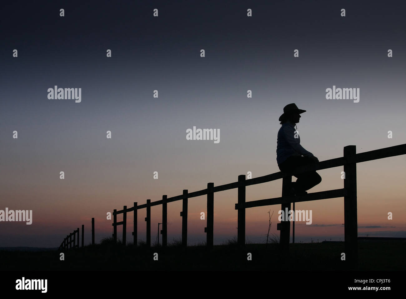 Cowgirl bei Sonnenuntergang am Zaun sitzen. Stockfoto