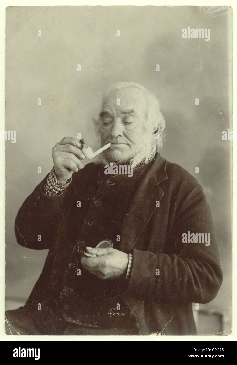 Porträt eines älteren viktorianischen Herrn, der Tabak in eine Tonpfeife aus einem Studio in Liskeard, Cornwall, England, Großbritannien, legt Stockfoto