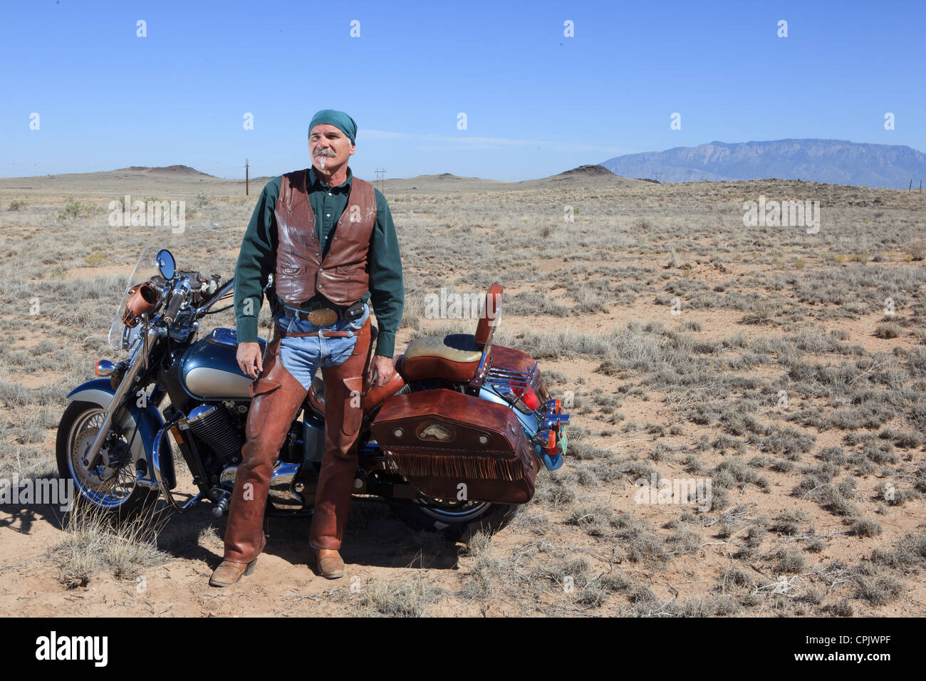 Ältere kaukasischen Mann tragen braune Leder stand neben seinem Motorrad in der Wüste. Stockfoto