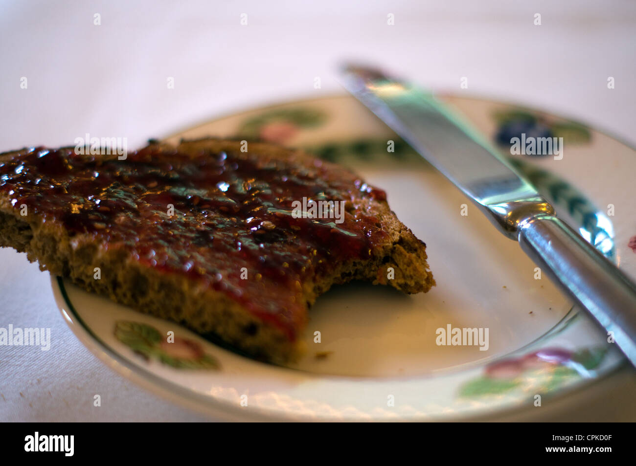 Eine Scheibe Brot Kornspeicher erstickt in Erdbeer-Gelee (Marmelade) mit einem Biss mit einem Messer auf einen Teller herausgenommen Stockfoto