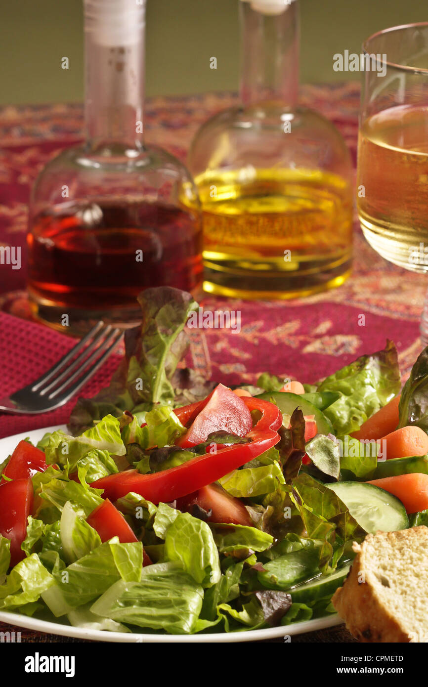 Ein Teller mit gemischter Salat und Gemüsesalat mit einer Menage aus Öl und Essig, Wein, Gabel, auf einem rosa print Tischset. Stockfoto