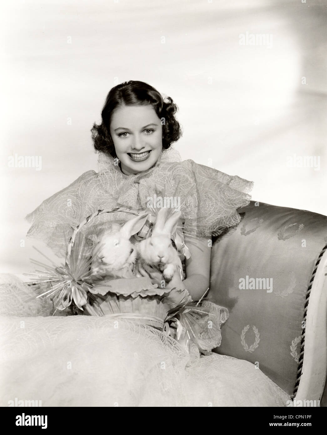 Lächelnde Schönheit mit zwei Kaninchen in einem Osternest Stockfoto