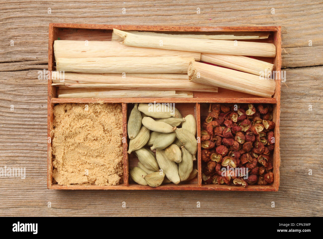 Kräuter und Gewürz, Zitronengras, Ingwer gemahlen, Kardamomsamen und Pfefferkörner in einem Holztablett auf einem Hintergrund von verwittertem Holz Stockfoto