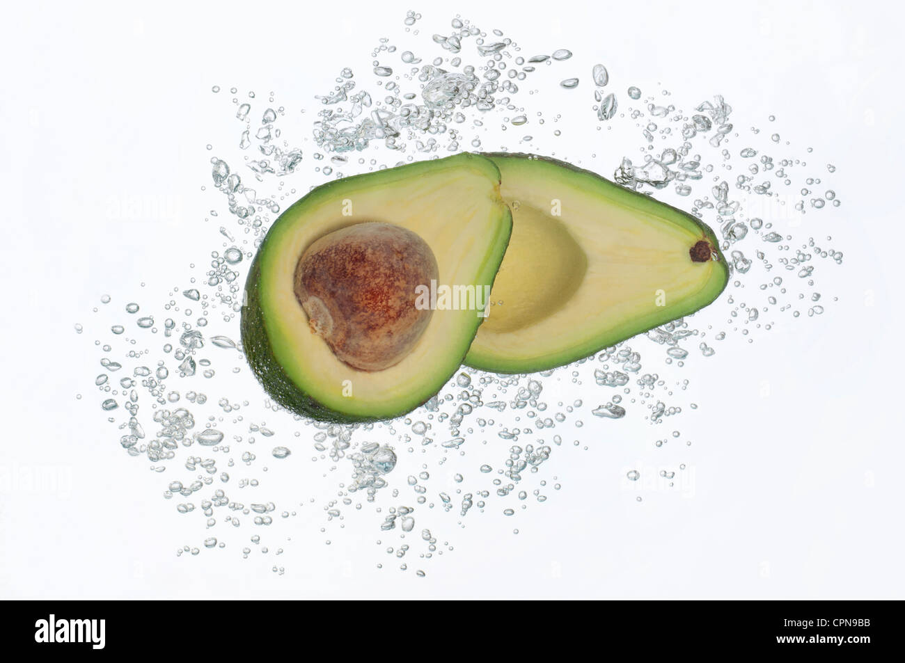 Avocado-Hälften untergetaucht im Wasser mit Kohlensäure Stockfoto