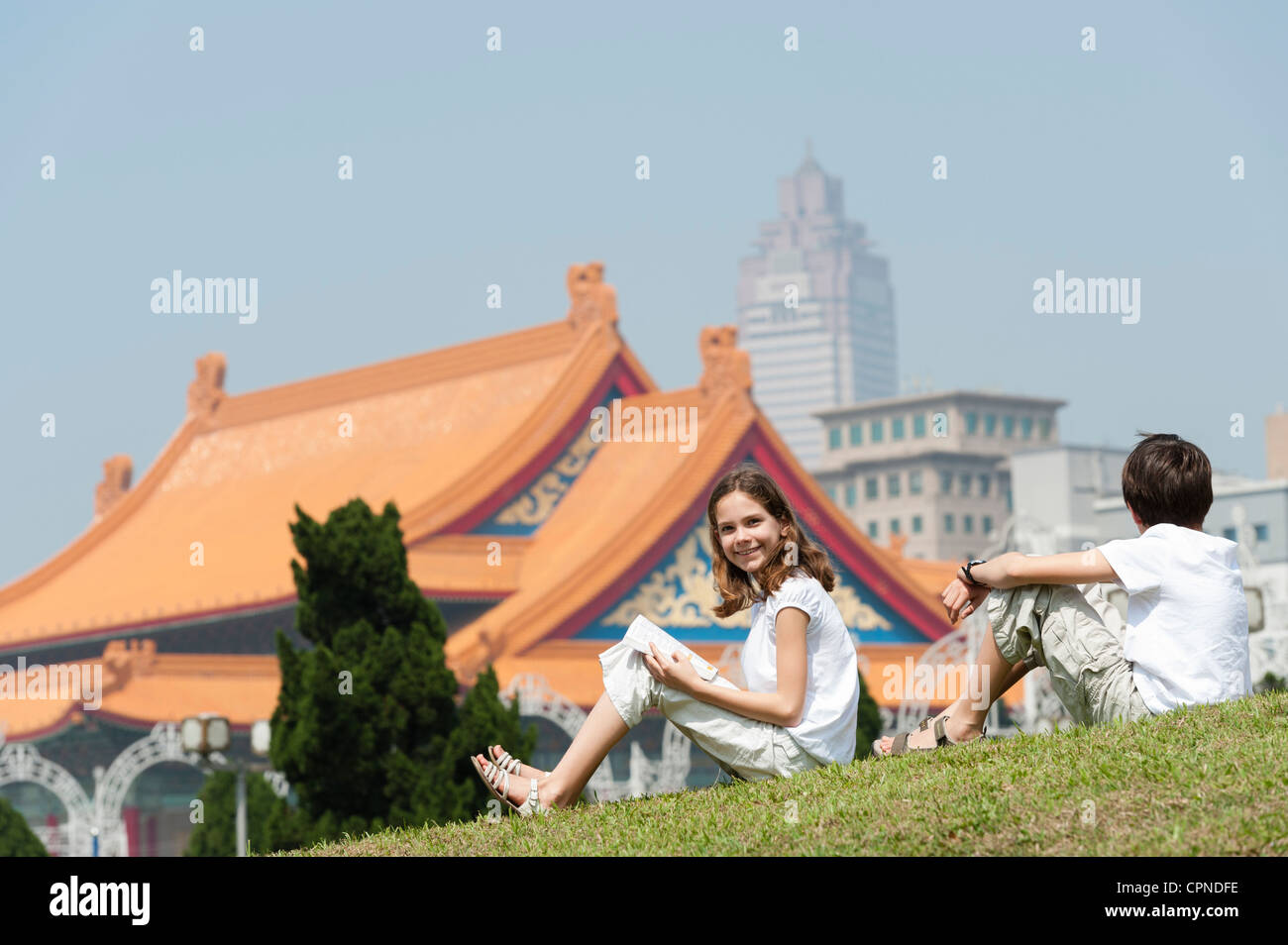 Mädchen sitzen auf dem Rasen mit Bruder in der Nähe von National Concert Hall, Chiang Kai-Shek Memorial Hall, Taipei, Taiwan Stockfoto