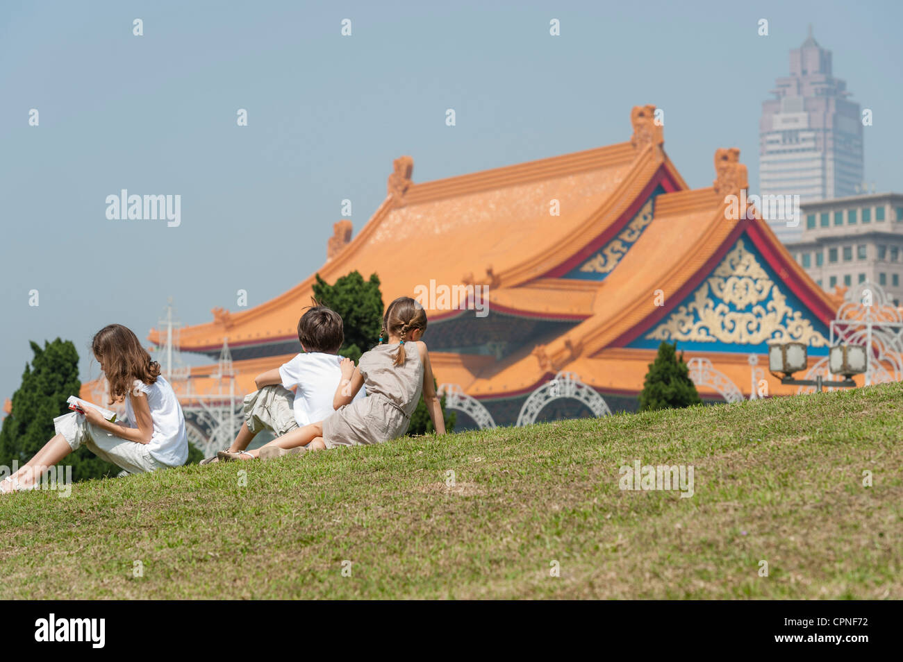 Kinder sitzen auf dem Rasen mit Blick auf die National Concert Hall, Chiang Kai-Shek Memorial Hall, Taipei, Taiwan Stockfoto