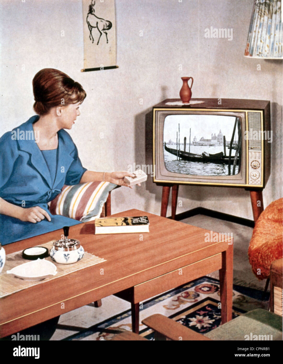 Fernsehsendung, Zuschauer, Frau mit Fernbedienung im Wohnzimmer, Fernsehgerät Loewe Opta, Atlanta, Tischgerät mit angeschraubten Beinen, Bildschirmgröße: 59 Zentimeter, Chassis: Feine Holzfurniere, Leinwandbild Venedig, Deutschland, 1962, Zusatzrechte-Clearences-nicht vorhanden Stockfoto