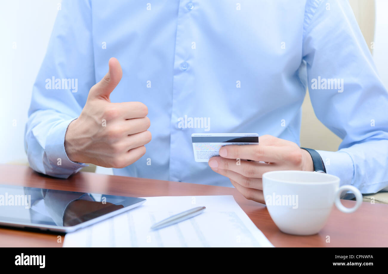 Erfolgreicher Geschäftsmann mit einer Kreditkarte in der Hand, sitzt am Arbeitsplatz. Stockfoto