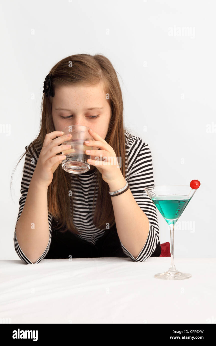 Ein neunjähriges Mädchen, das Limonade trinkt, während er einen alkoholischen Cocktail betrachtet Stockfoto