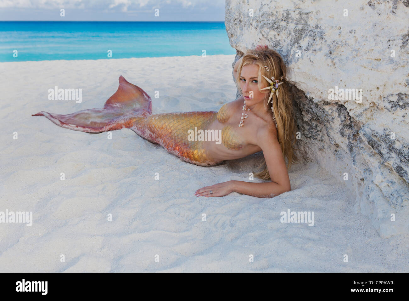 Junge blonde Meerjungfrau Verlegung im Schatten eines großen Felsens am Strand von Cancun Mexiko. Stockfoto