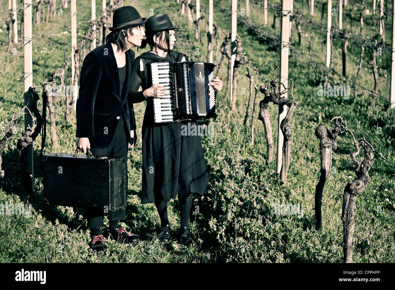 ein Vagabund paar stehend auf einem Feld mit Reben, er hat einen Leder-Koffer, sie spielt auf einem Akkordeon Stockfoto