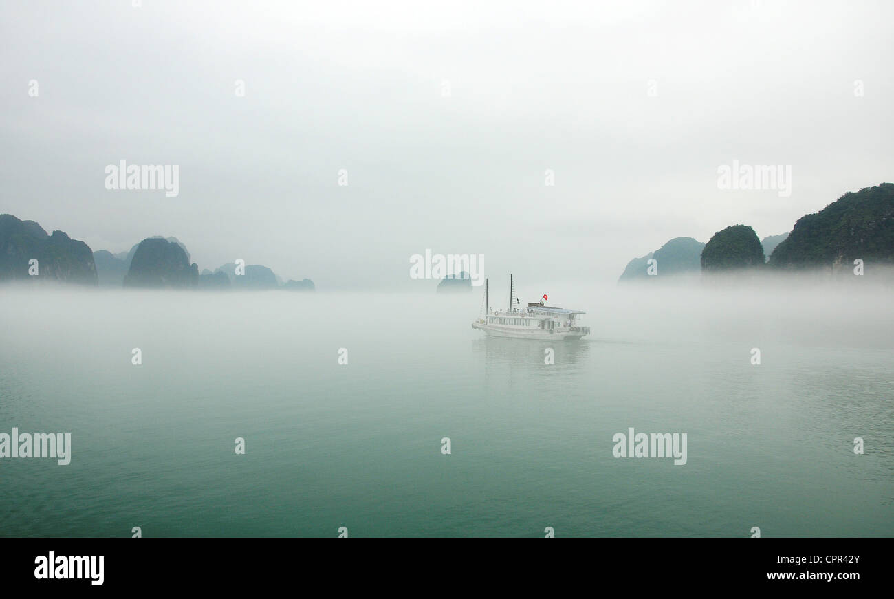 Ein einsamer Schiff reist durch einen nebligen Ha Long Bucht, Vietnam. Stockfoto