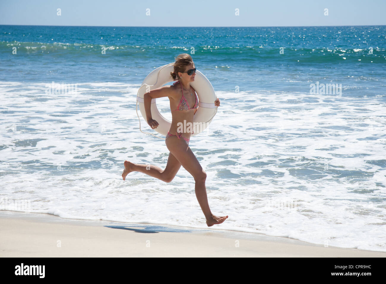 Junge Frau am Strand mit einem weißen Rettungsring auf quer Stockfoto