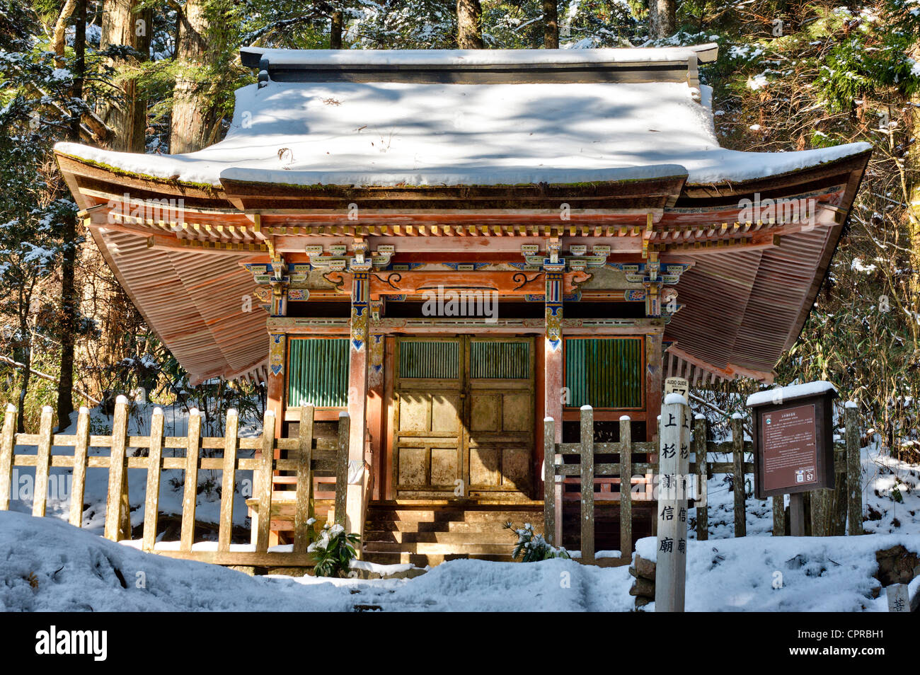 Der berühmte Friedhof von Okunoin in Koya in Japan. Schneebedeckte hölzerne, bemalte Mausoleum-Halle, die das Grab von Uesugi Kenshin mit Zedern hinter sich markiert. Stockfoto