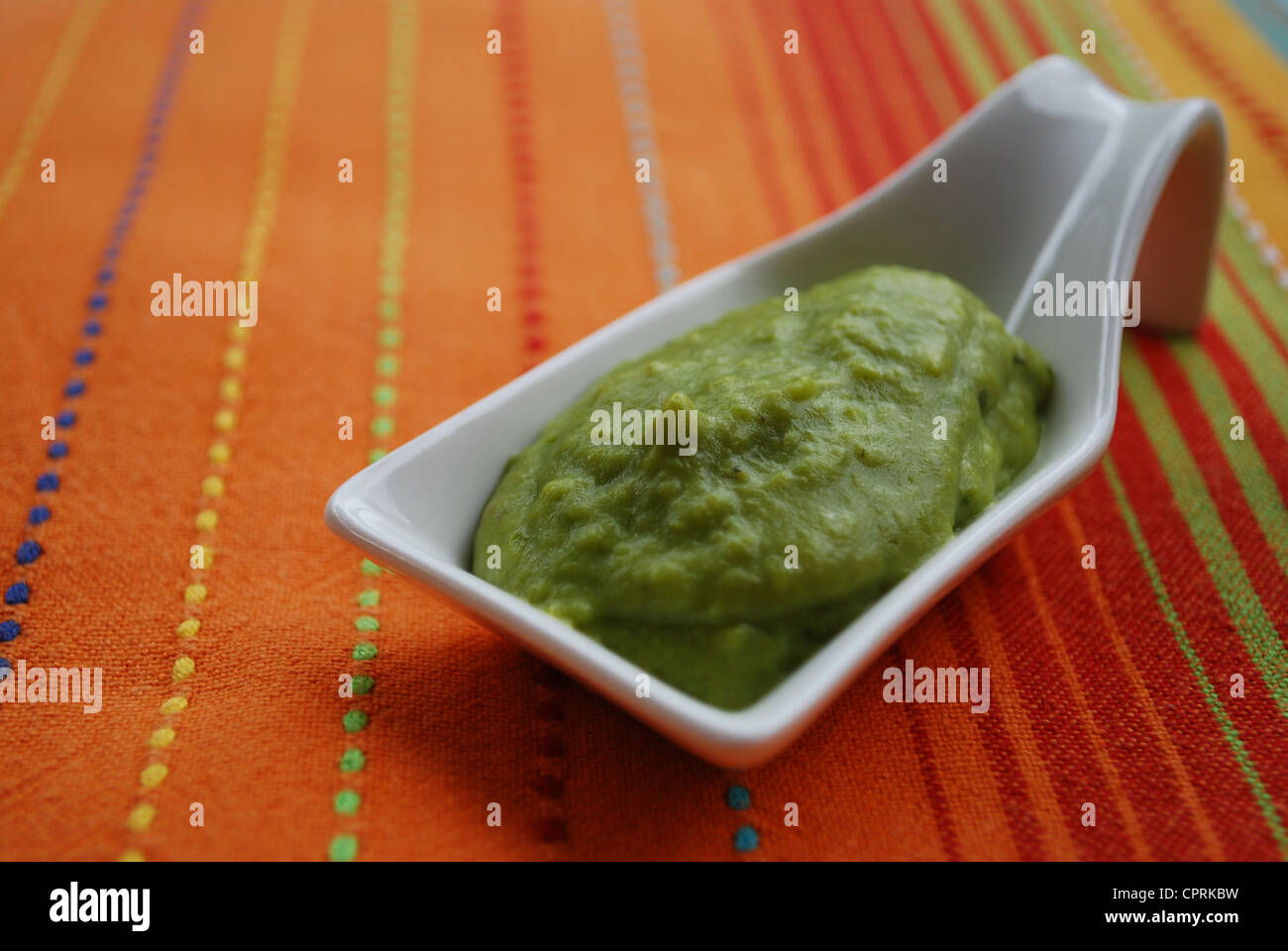 Grüne Bohnen Sahne mit Basilikum in Weißware Schale auf orange Stoff Hintergrund Stockfoto