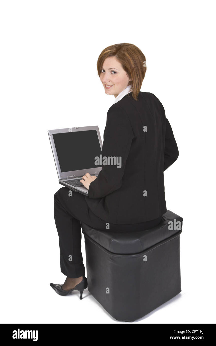 Geschäftsfrau auf Pouf mit einem Laptop auf dem Schoß sitzen und blickte zurück über die Schulter. Stockfoto