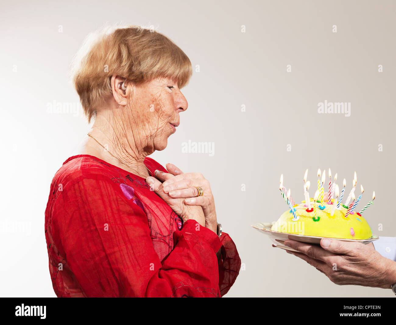 Ältere Frau empfangen Geburtstagskuchen vor weißem Hintergrund Stockfoto