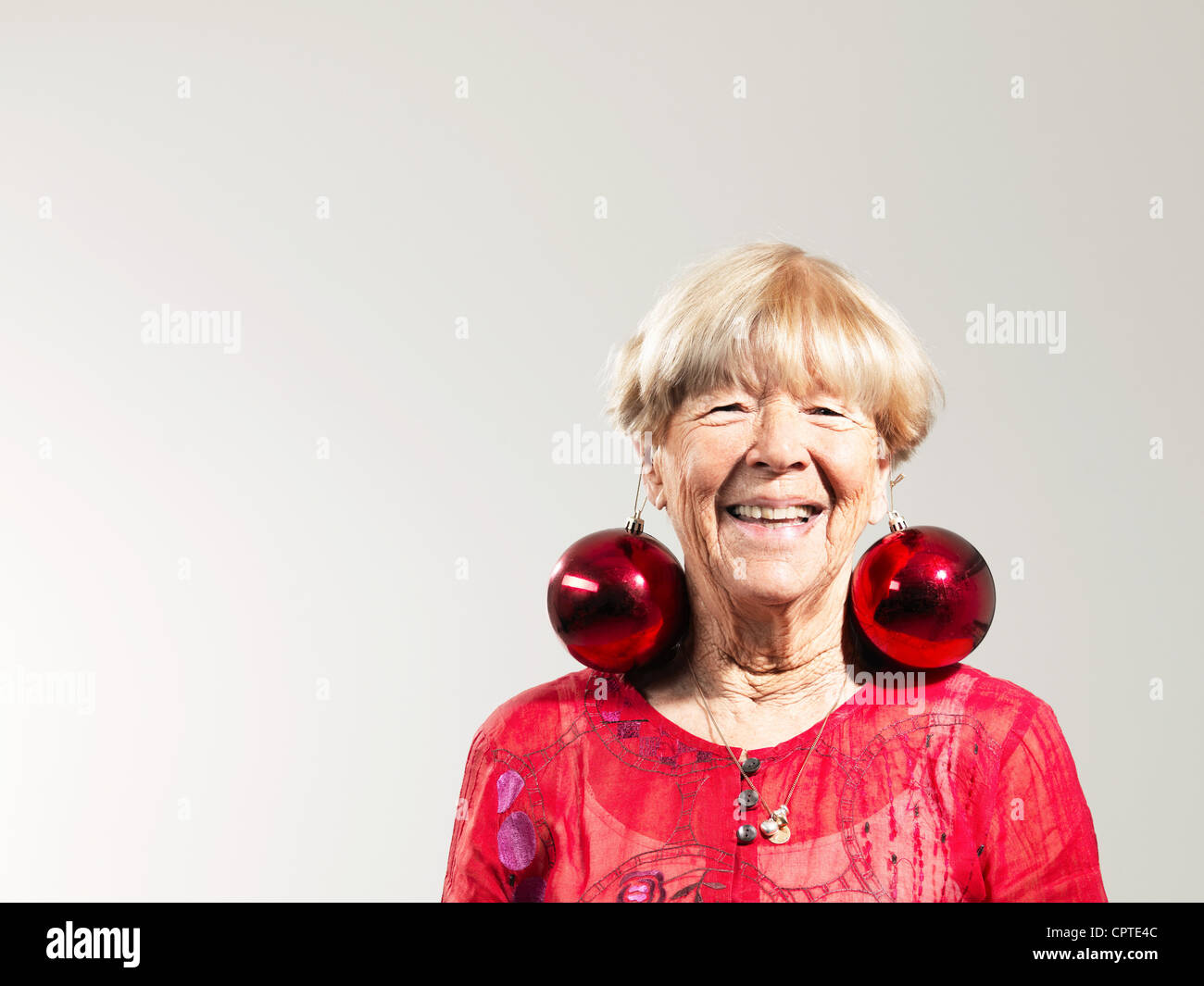 Senior Frau mit roten Kugeln als Ohrringe vor weißem Hintergrund Stockfoto