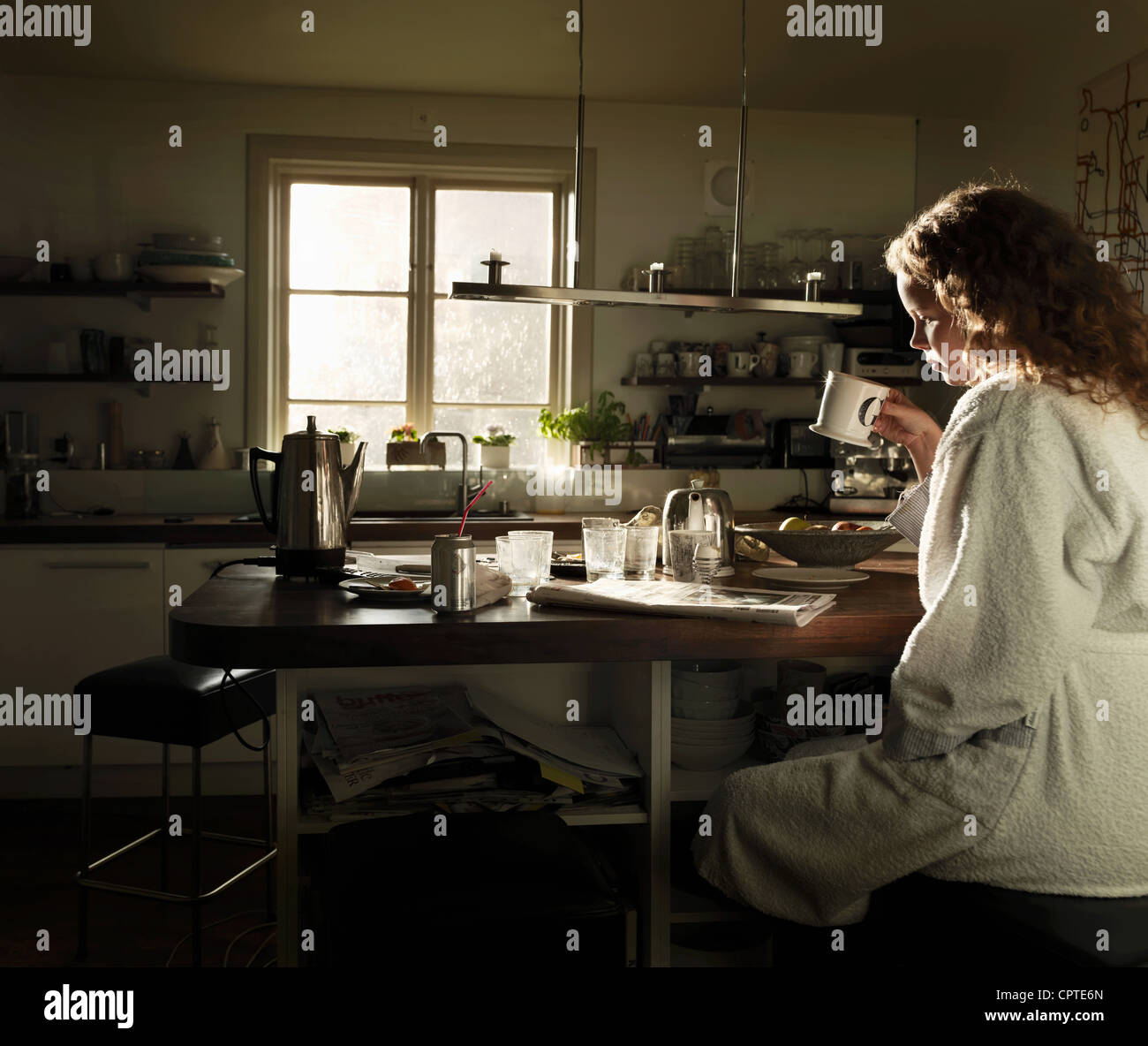 Junge Frau, die Zeitungslektüre am Küchentisch beim Frühstück Stockfoto