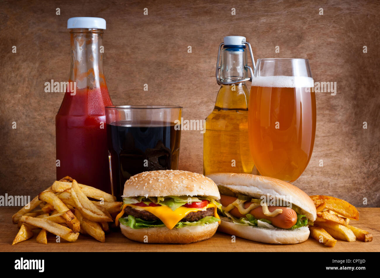 Junk-Food mit Burger, Würstchen, Pommes, Cola, Ketchup und Bier auf einem hölzernen Hintergrund Stockfoto