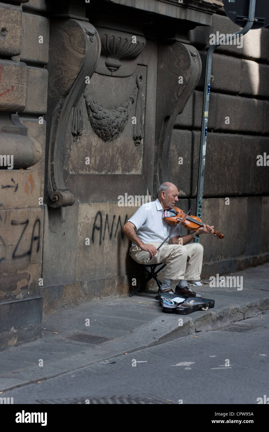 Ein Straßenmusikant seine Geige zu spielen, in den Gassen von Florenz, umgeben von Graffiti und gebeizt Gebäude Stockfoto