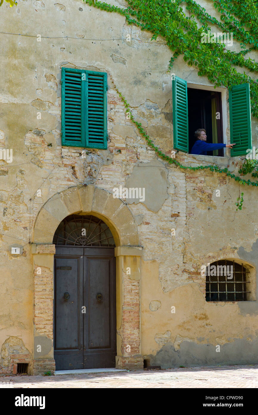 Frau öffnet Fensterläden des Hauses in Hügel Stadt Monticcheillo, Val D'Orcia Gegend der Toskana, Italien Stockfoto