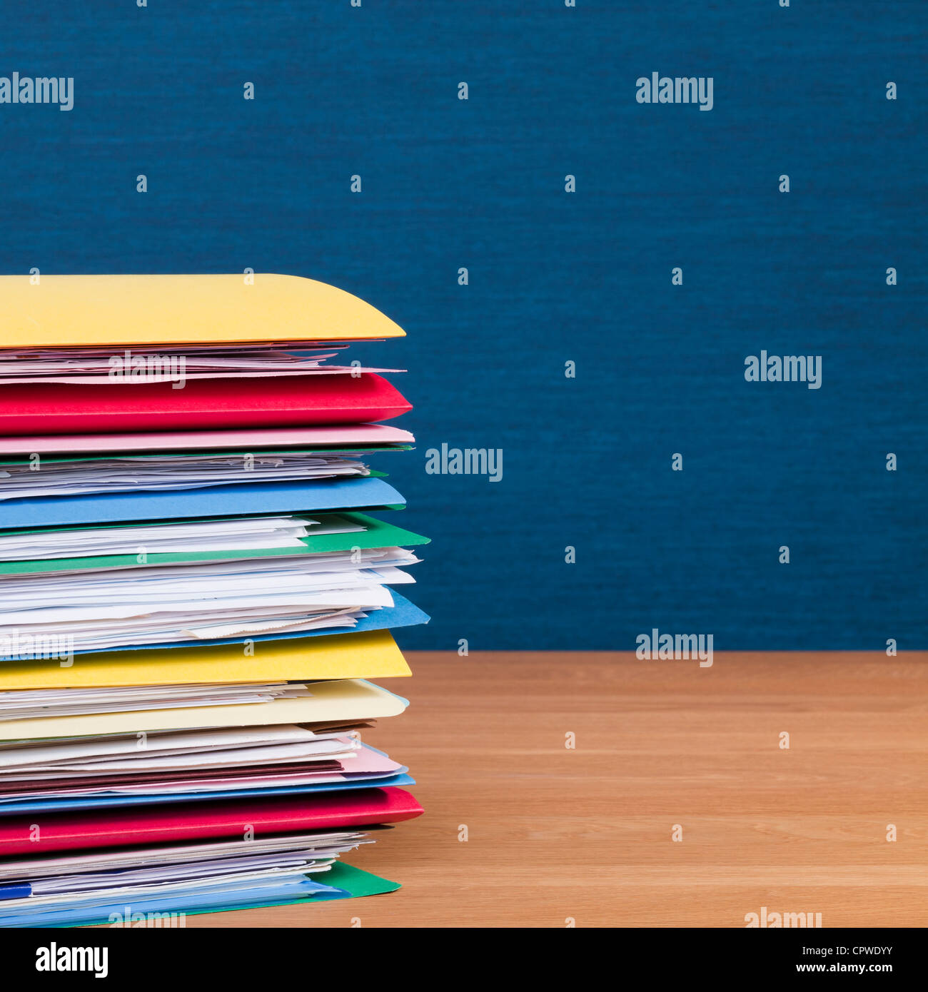 Hohe Stapel voller Papierkram, Dateien auf einer Holzfläche mit einer blauen Wand hinter. Kopieren Sie Raum. Stockfoto