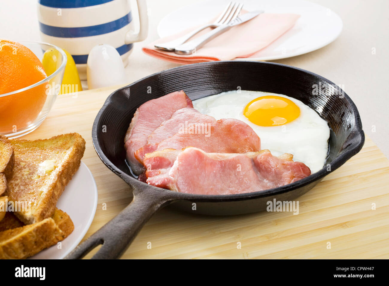 Speck und Ei Frühstück in einer gusseisernen Pfanne erhitzen und einen Teller mit Toast. Stockfoto