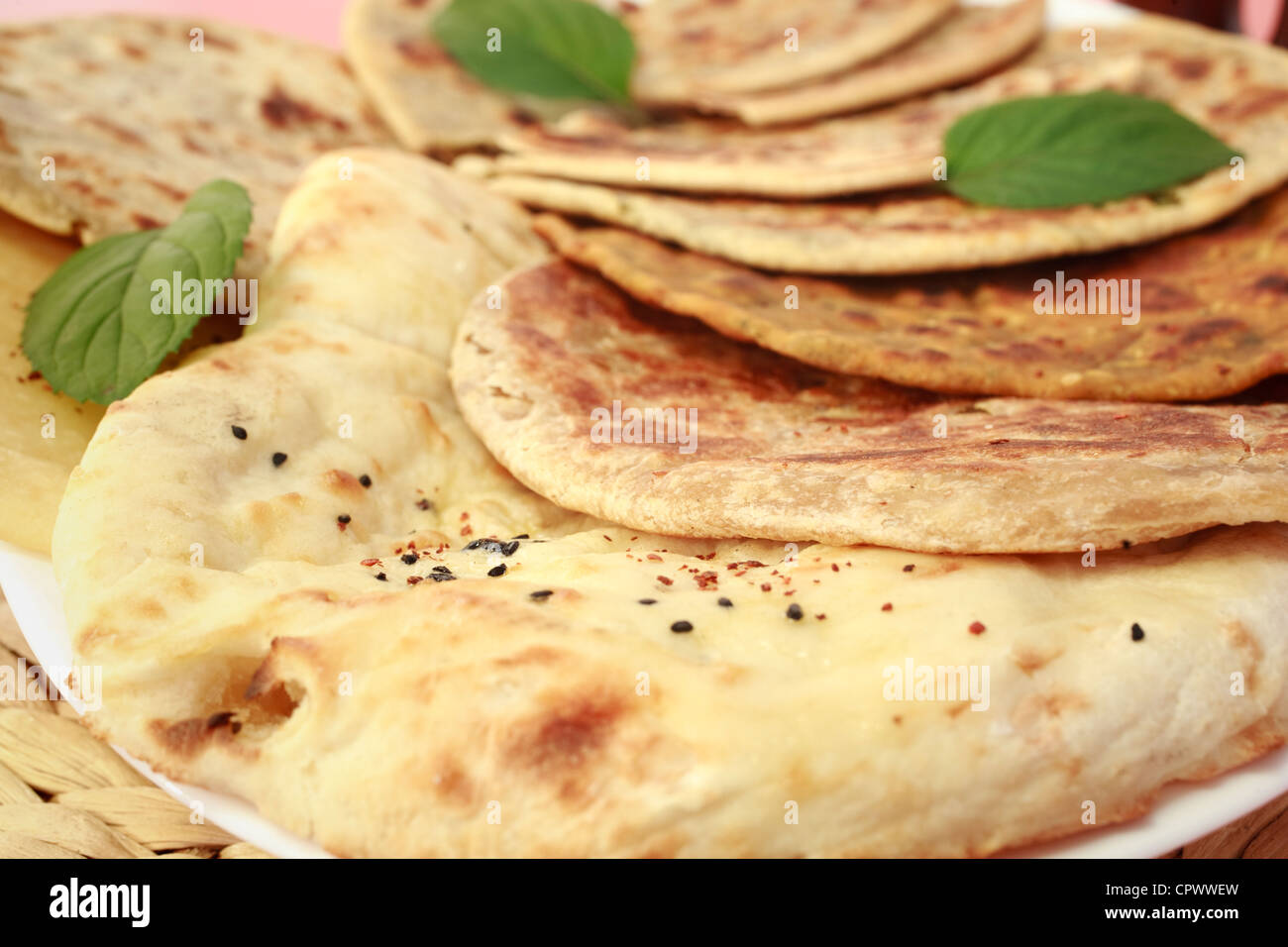 Auswahl an indischen Brotsorten mit Naan in den Vordergrund und verschiedene gefüllte Parathas hinter, garniert mit Minze Blätter Stockfoto