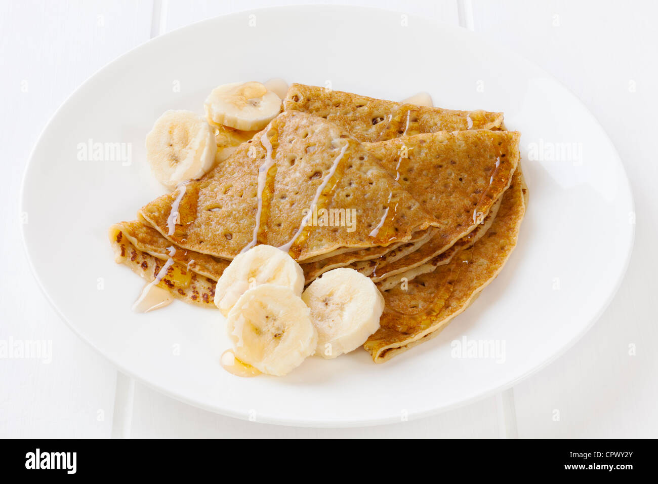 Ein Teller mit Crêpes oder Pfannkuchen mit in Scheiben geschnittenen Banane und Ahornsirup. Stockfoto