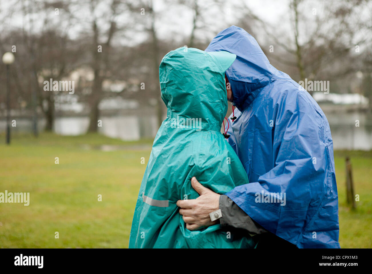 Älteres Paar in wasserdichte Kleidung küssen im park Stockfoto