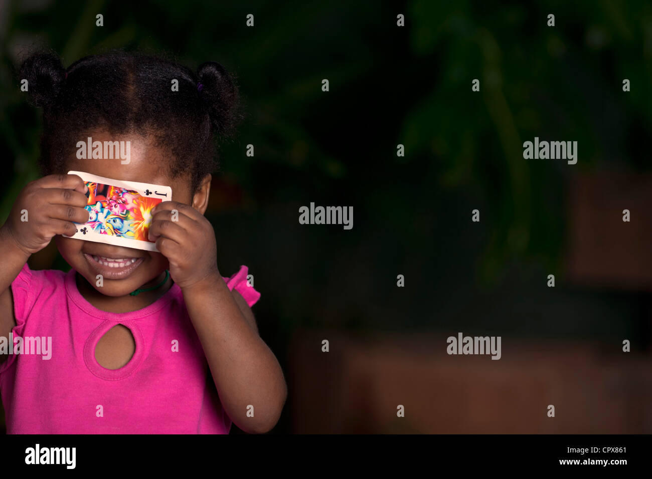 Junge schwarze Mädchen hält eine Spielkarte über ihre Augen Stockfoto